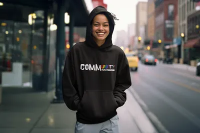 COMMUNITY OVER FASCISM-pullover-hoodie-mockup-of-an-ai-generated-happy-woman-standing-on-a-sidewalk-m36036